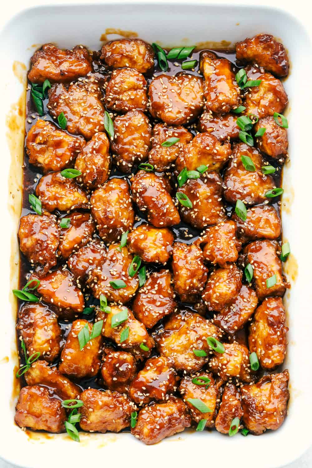 Sesame Chicken is sweet, savory, and perfect for any night of the week. This is so good, it is even better than take out! Baked honey sesame chicken in a white dish.