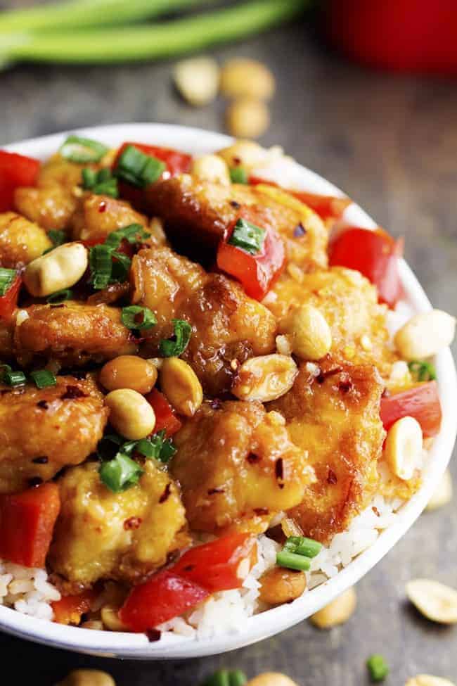 Delicious breaded chicken coated in a sweet and spicy sauce with peppers and peanuts hidden throughout. This is WAY better than any takeout you will have! Baked Kung Pao chicken over white rice in a bowl.