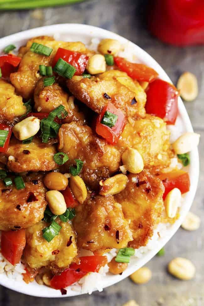 Delicious breaded chicken coated in a sweet and spicy sauce with peppers and peanuts hidden throughout. This is WAY better than any takeout you will have! Baked Kung Pao chicken in a bowl with white rice and garnished with peanuts.