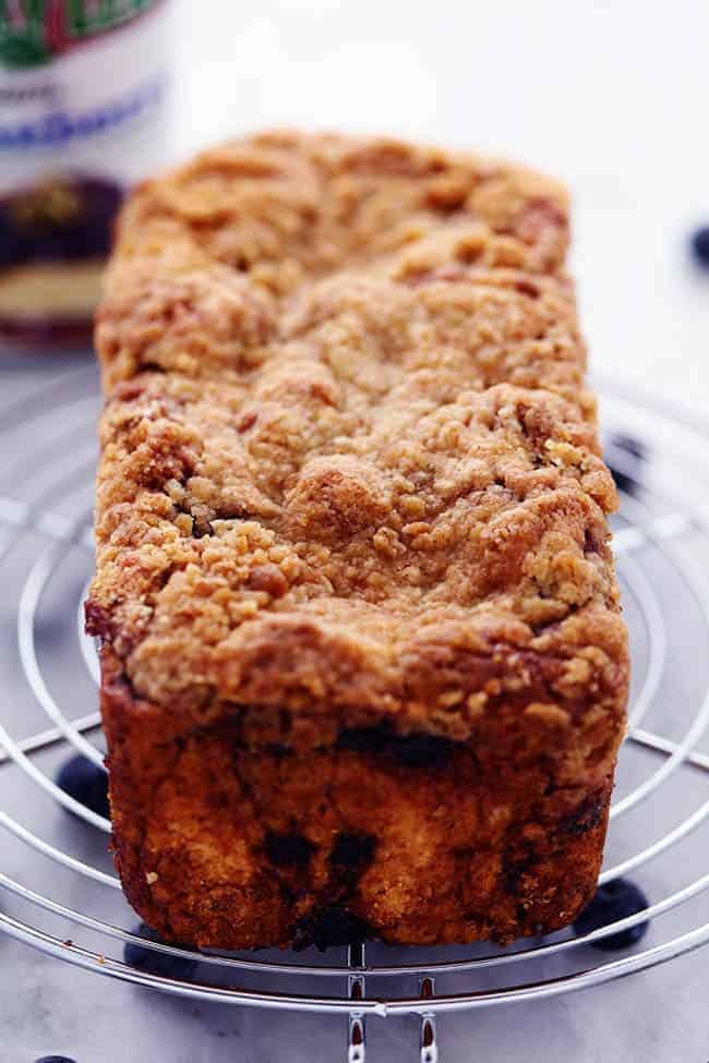An amazingly moist muffin bread filled with blueberry pie filling. Topped with a crumb topping and drizzled in a lemon glaze this bread is incredible! Blueberry pie bread on a cooling rack fresh out of the oven.
