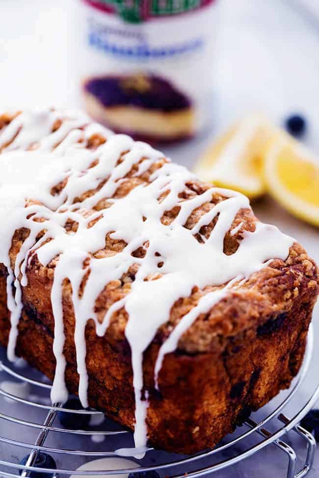 An amazingly moist muffin bread filled with blueberry pie filling. Topped with a crumb topping and drizzled in a lemon glaze this bread is incredible! Blueberry pie bread on a cooling rack with fresh lemon glaze.