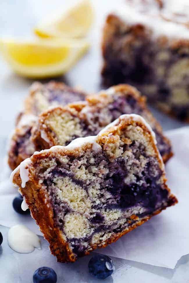 An amazingly moist muffin bread filled with blueberry pie filling. Topped with a crumb topping and drizzled in a lemon glaze this bread is incredible! Slices of blueberry pie bread with lemon glaze and fresh blueberries on the side.