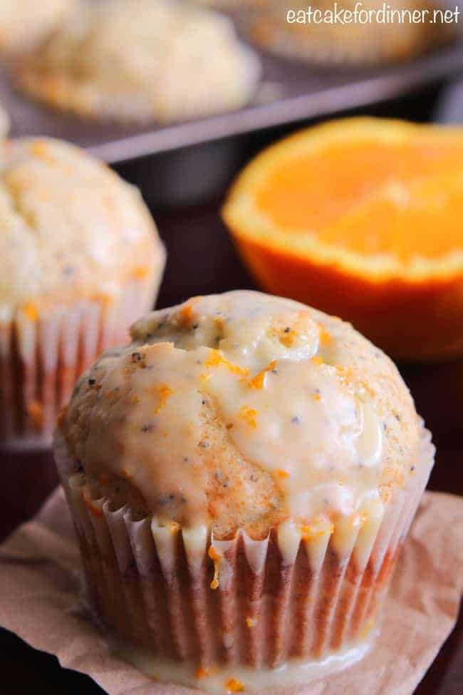 A delicious banana poppy seed muffin that bakes perfectly moist. The orange glaze adds such a unique and delicious glaze on the top and will become a new favorite! Banana Poppy Seed Muffins with an Orange Glaze and a fresh cut orange in the background.