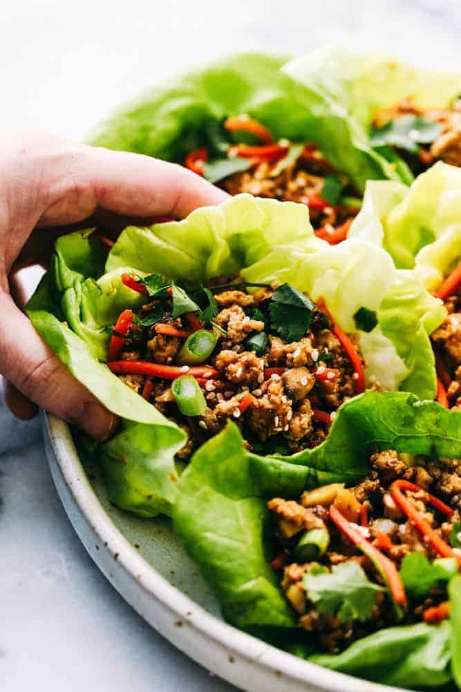 Asian turkey lettuce wraps are packed with intense flavor from tender meat and seasoned, crunchy veggies. These light and tasty wraps are the perfect healthy appetizer or even dinner! Asian lettuce wraps with a hand picking one up.