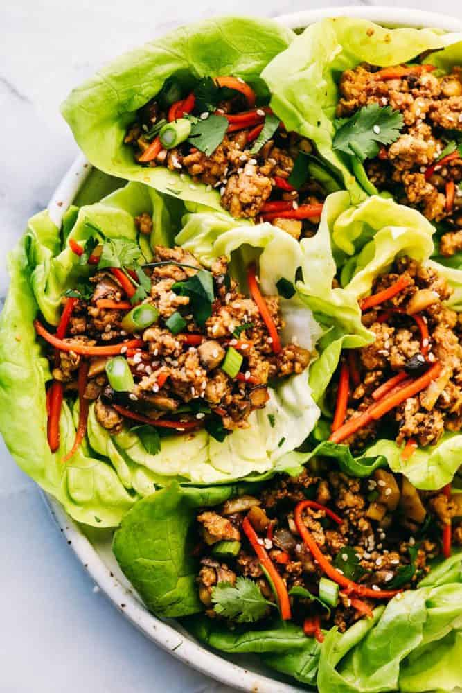 Asian turkey lettuce wraps are packed with intense flavor from tender meat and seasoned, crunchy veggies. These light and tasty wraps are the perfect healthy appetizer or even dinner! Asian turkey lettuce wraps on a white plate.