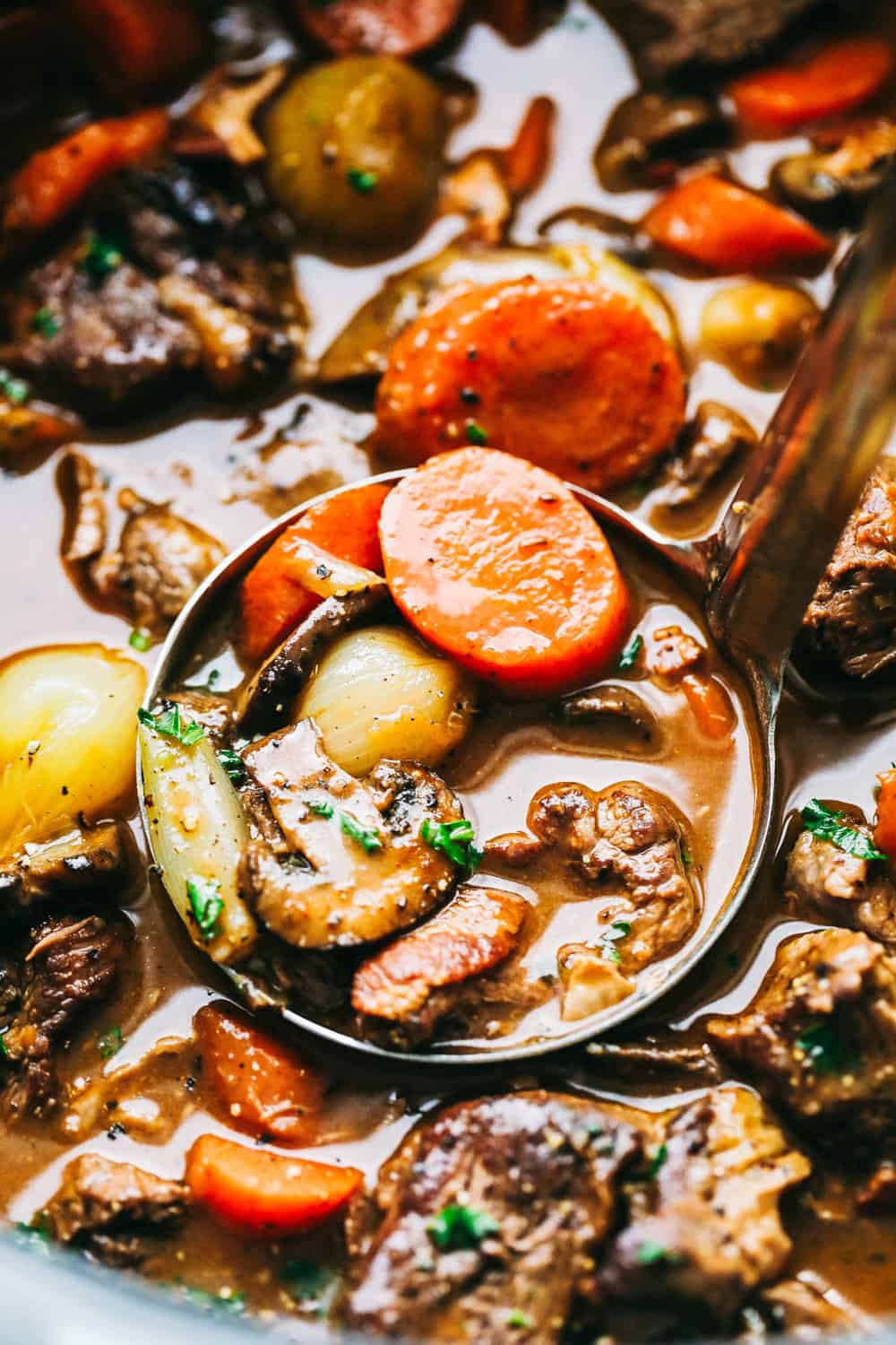 Beef Bourguignon is a French classic made with melt in your mouth beef, mushrooms, carrots, and red wine and is cooked to perfection in the most delicious rich sauce. A hearty and comforting meal that you will make again and again! Beef Bourguignon being scooped into a ladle.