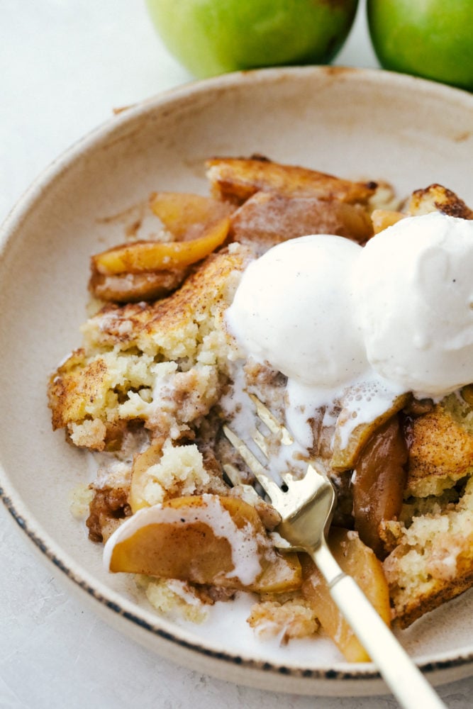 Old Fashioned Apple Cobbler is a warm baked fruit dessert that is topped with a perfect biscuit-like crust. The warm cinnamon spice is comforting and satisfying and nails a perfect summer dessert! Apple cobbler on a plate topped with vanilla ice cream.
