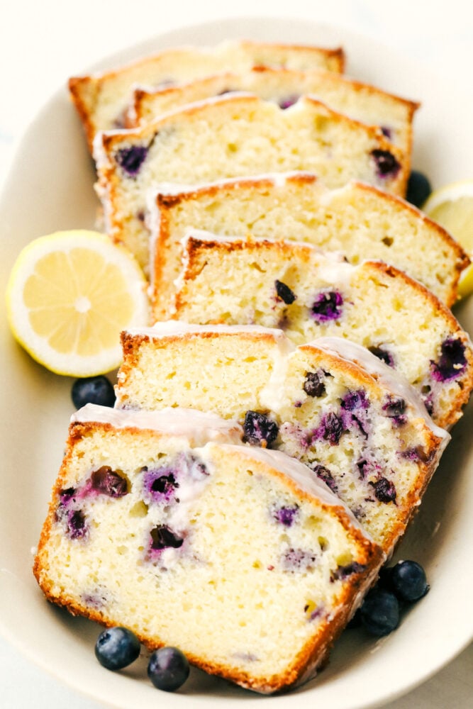 Blueberry Lemon Pound Cake! This pound cake is made lighter by using greek yogurt, and is loaded up with lemon flavor thanks to zest and fresh lemon juice! Juicy blueberries are baked right in. All drizzled with a luscious lemon glaze. Slices of the cake with lemon glaze on a plate.