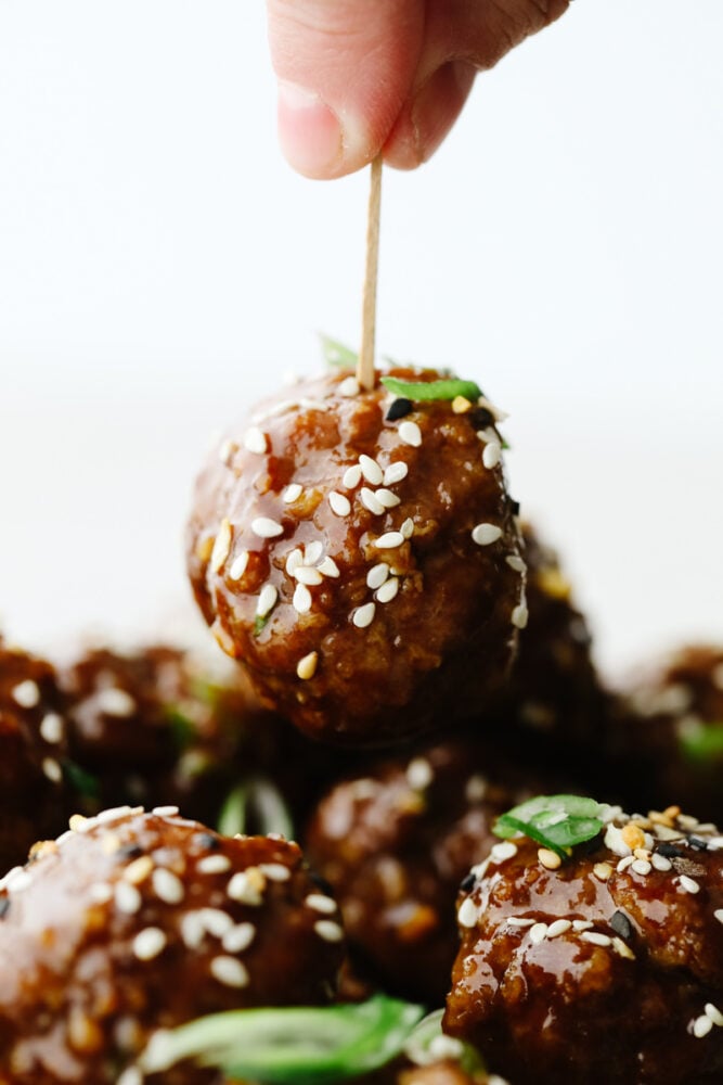 These saucy Asian meatballs are the perfect blend of flavors and are drenched in the most insanely delicious sauce! Perfect for dinner or even an appetizer, they will certainly get a "WOW!" at your next get-together! A toothpick being poked into a meatball.